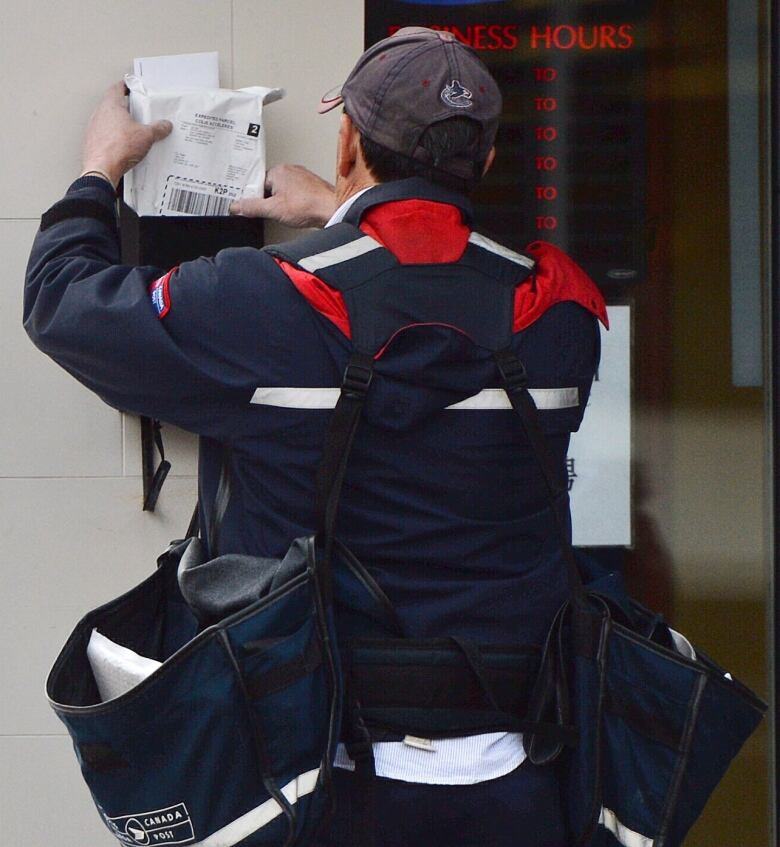 A Canada Post employee puts mail in a mailbox.