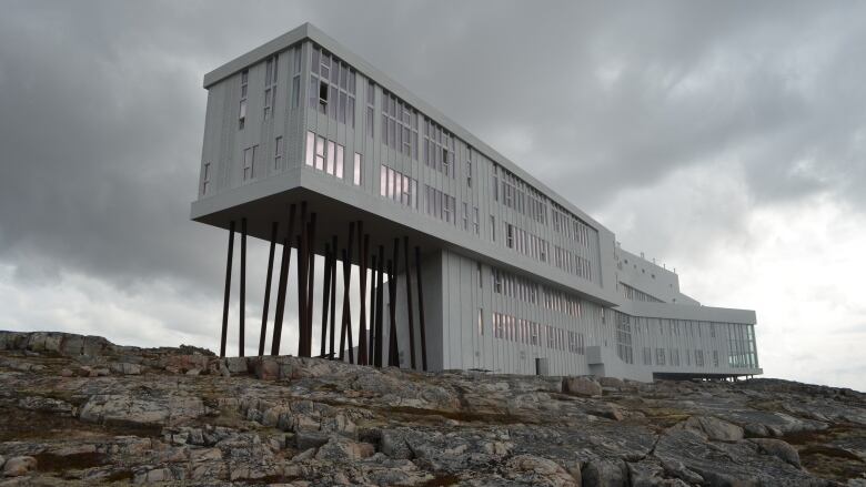 A large hotel sits on a layer of rock. Part of the building is held up by a series of beams.