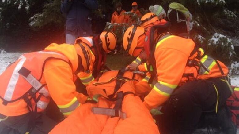 A group of people wearing reflective orange equipments lifts an orange gurney.