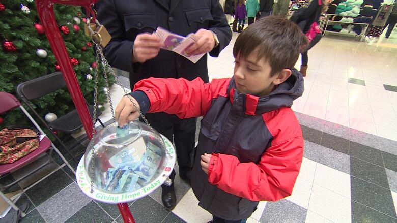 A little boy puts money into a charity kettle.