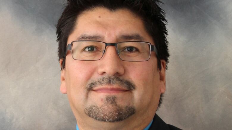 A headshot of a man with dark hair and a blue dress shirt and dark tie.