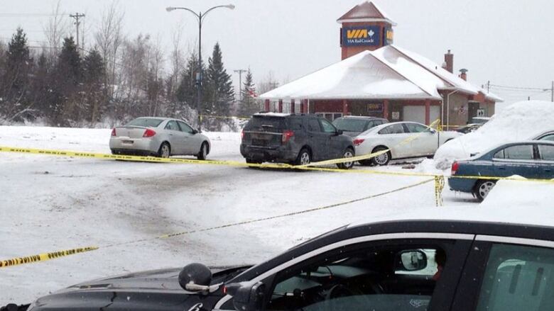 A snowy scene with multiple vehicles behind yellow police tape with a train station in the background.