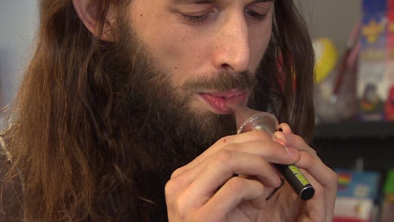 A man with long hair is shown using a vaporizer.