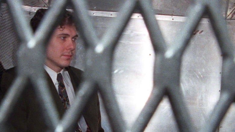 A man in a tie sits in a prison van.