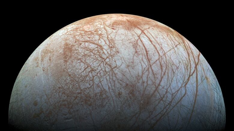 Jupiter's beige-coloured moon Europa, which is marked by brown zig-zagged lines, hangs in the blackness of space.