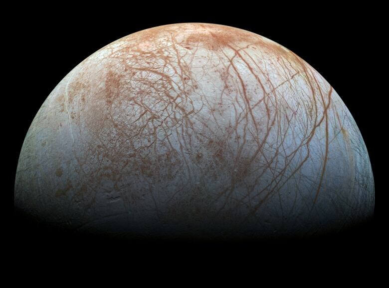 Jupiter's beige-coloured moon Europa, which is marked by brown zig-zagged lines, hangs in the blackness of space.