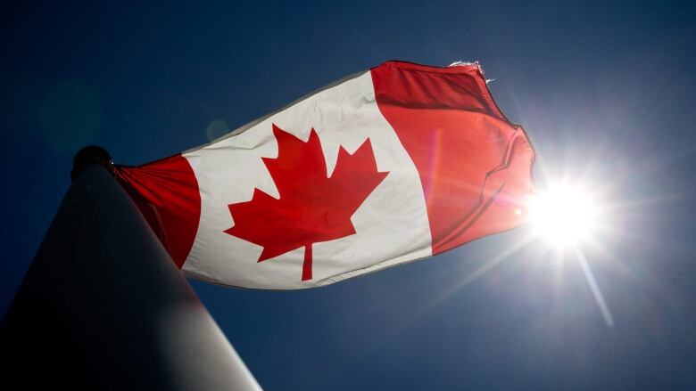 a Canadian flag flies at the top of a flagpole with a blue sky behind it