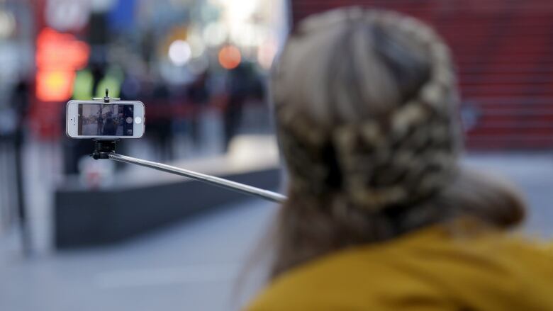 The back of a person holding a phone on a selfie stick.