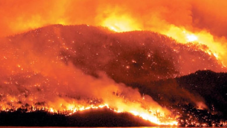 An orange fire rages out of control on a hillside at night.