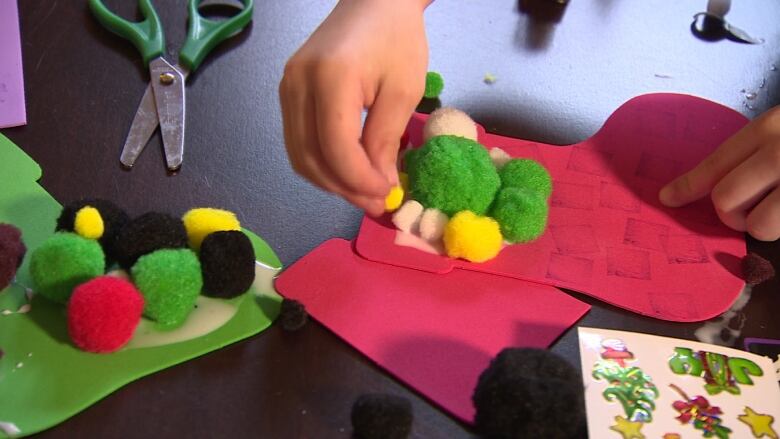 A child glues a pom-pom on to construction paper