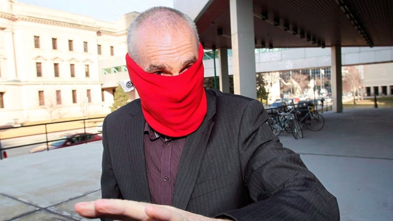 A man wearing a red neckwarmer covering his face exits the Winnipeg lawcourts. 