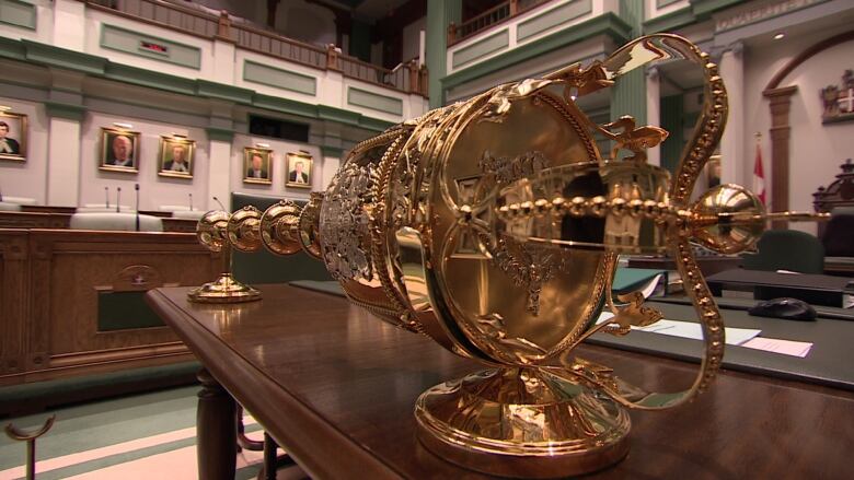 A golden House of Assembly mace sits on a wooden table.