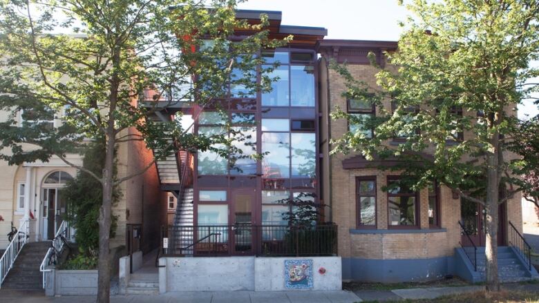 A three-storey social housing building made of shipping containers stands on a tree-lined Vancouver street.