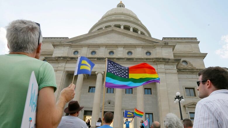 A crowd some with flag in hand stand in front of the capitol building in Little Rock, Ark.