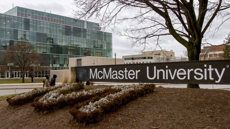 A sign that reads McMaster University atop a garden patch with a glass building in the background