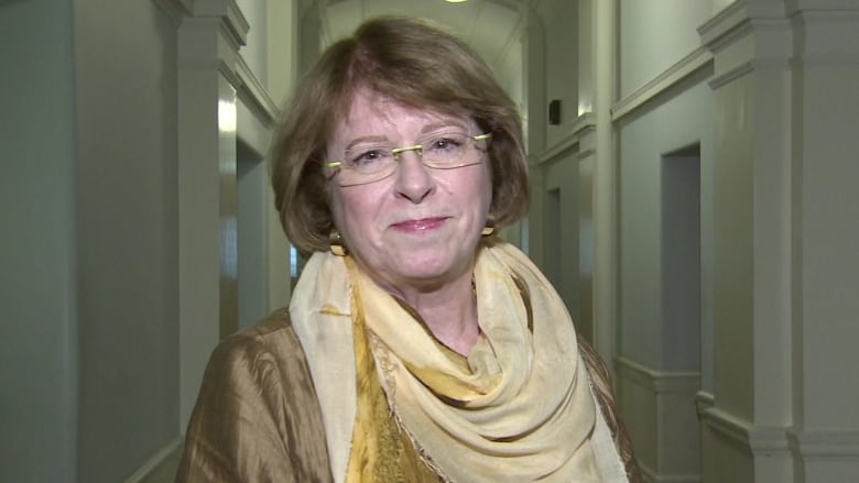 A woman wearing a gold-coloured dress speaks in a corridor.