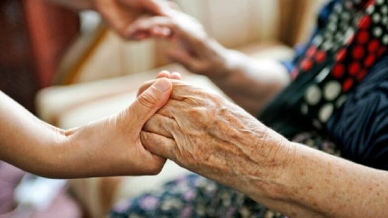 A caregiver holds the hands of a seated senior.