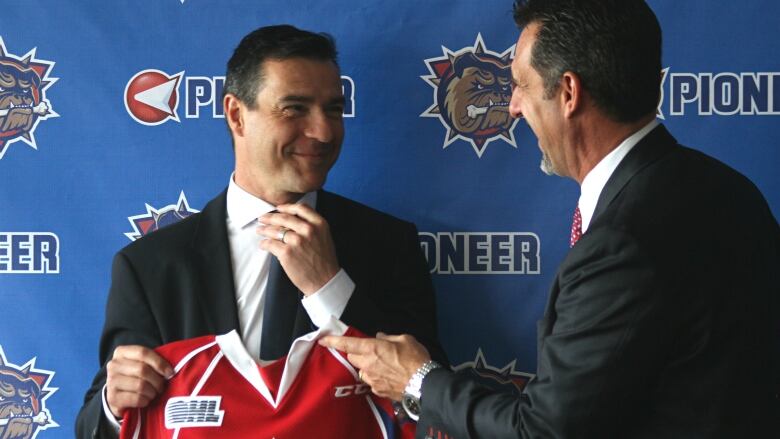 Two hockey team officials smile after a news conference.