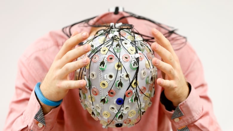 A person poses with an electroencephalography cap, which has a lot of wires .