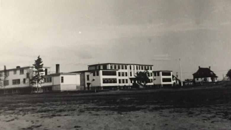 A black and white photo depicts a residential facility on a stretch of grass.