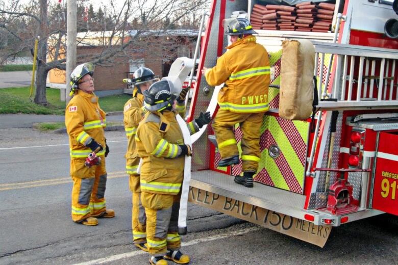 Firefighters wearing yellow fire gear stand near the back of a fire truck.