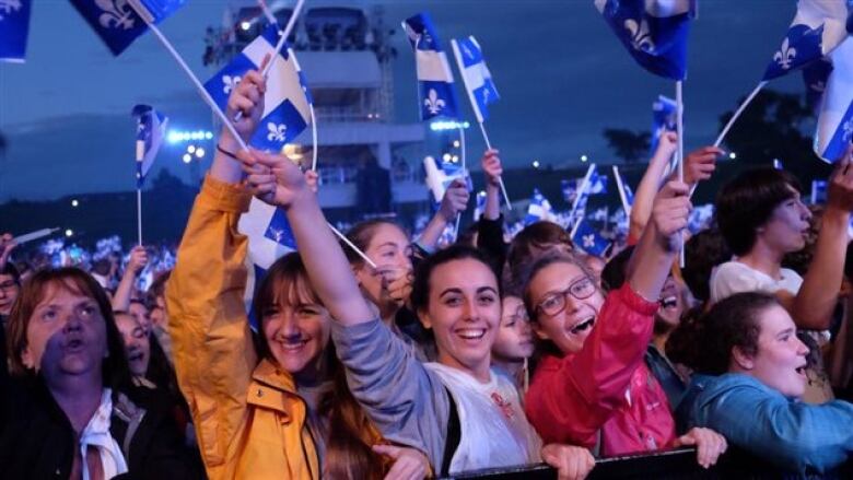 People at a concert waving Quebec blue-and-white flags.