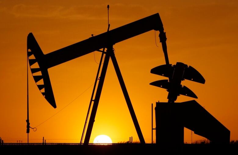 A photo of a pump jack in silhouette against the sun.