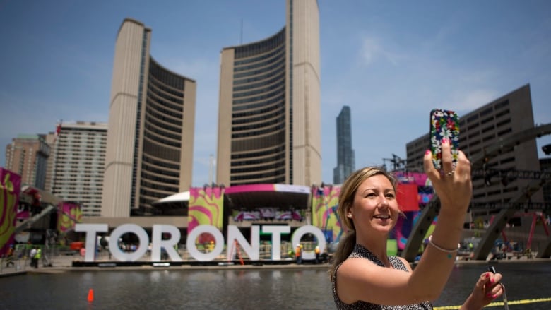 A woman takes a selfie in front of a large sign reading 