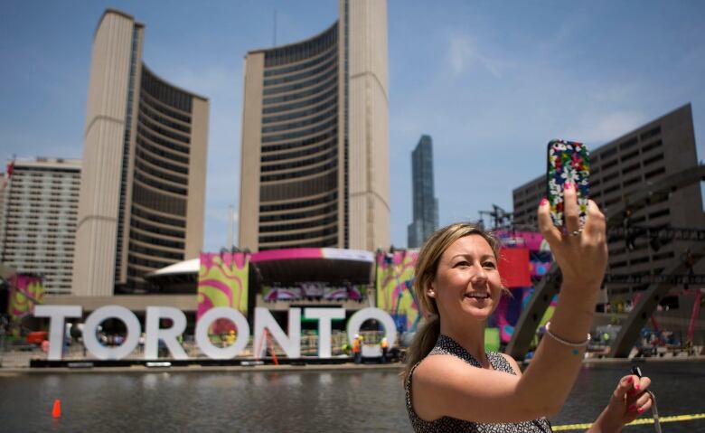 A woman takes a selfie in front of a large sign reading 