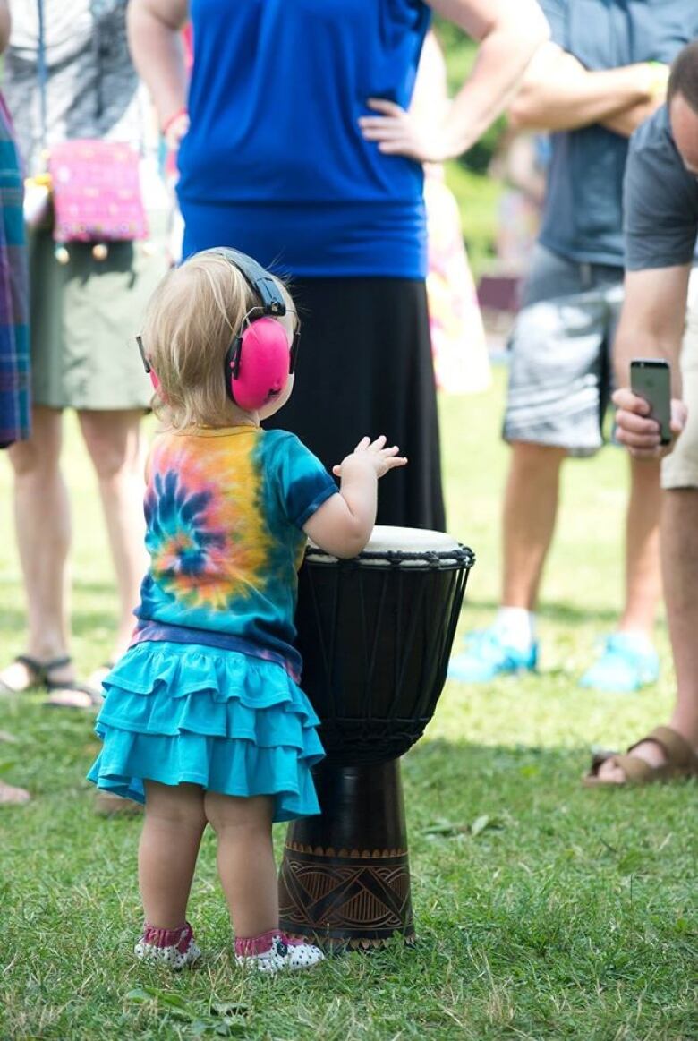 A child with protective headphones on faces away from camera and plays on a hand drum