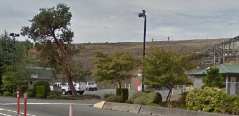 A road with a treed area off to the side, with signs for a landfill.