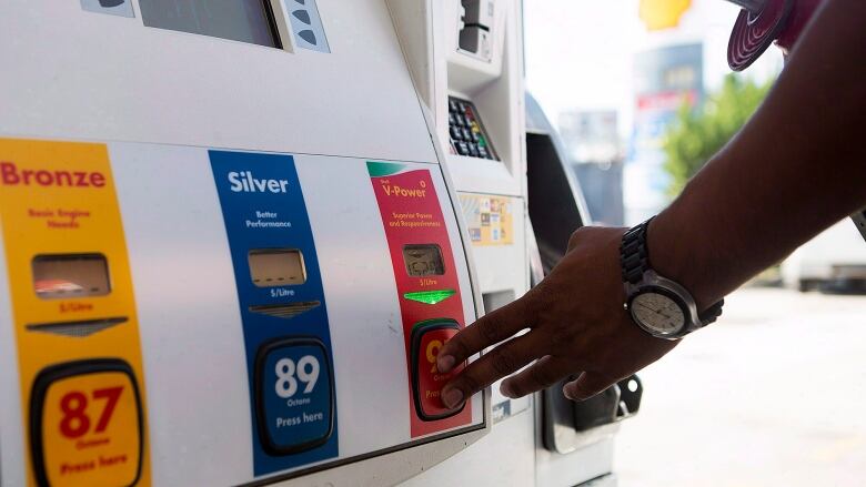 A hand presses a button at a gas pump.