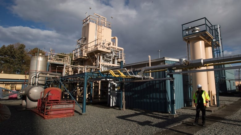 A worker in a hard hat walks in front of an industrial facility. 