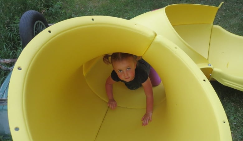 A little girl with pigtails peeks out of a yellow slide.