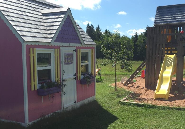 A pink play house in front of a playground.