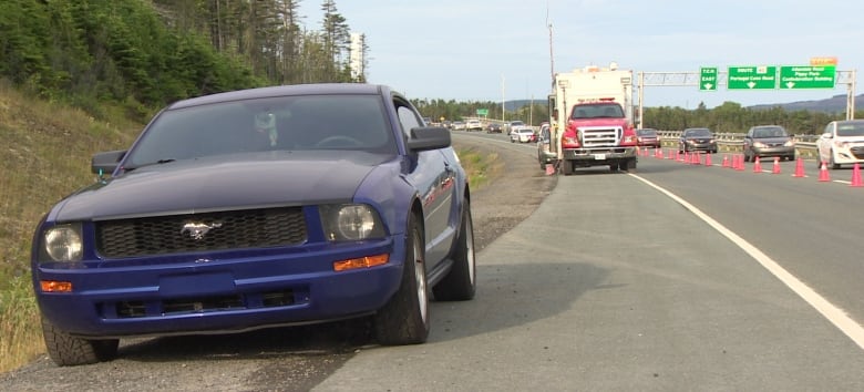 A blue car sits on the side of a busy road.