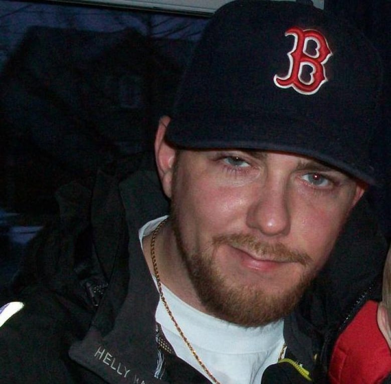 A young bearded man wears a baseball cap