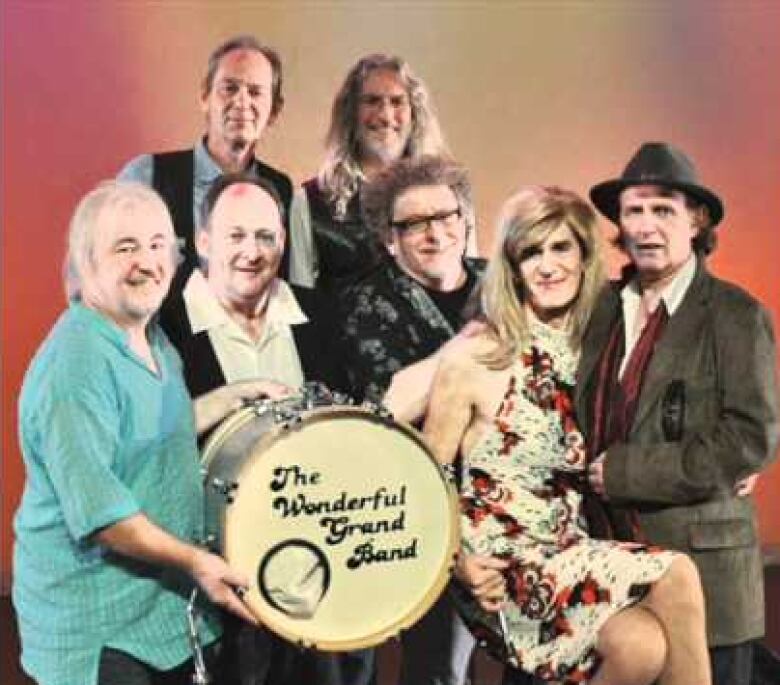 Seven people stand, holding a bass drum that reads The Wonderful Grand Band. 