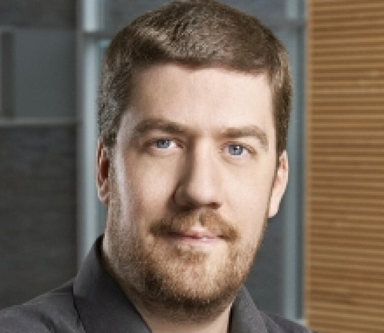 A headshot of a man with short brown hair and a mustache 