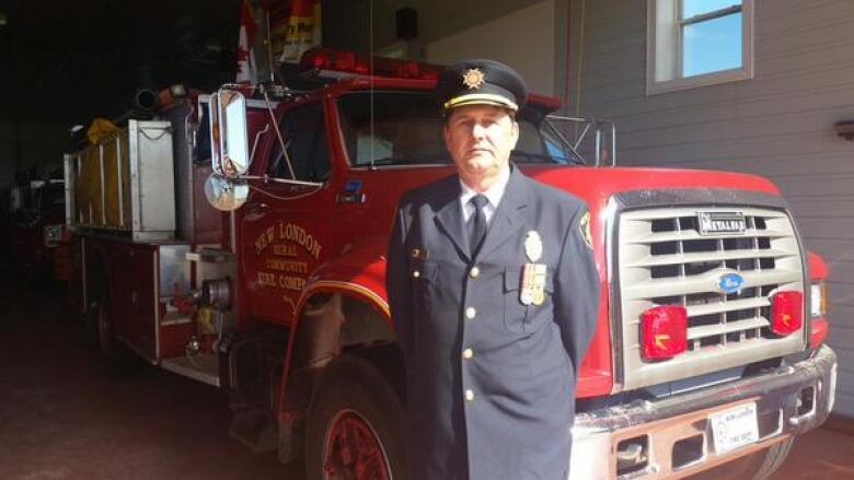 A man in a fire chief's uniform stands in front of a red fire engine. 