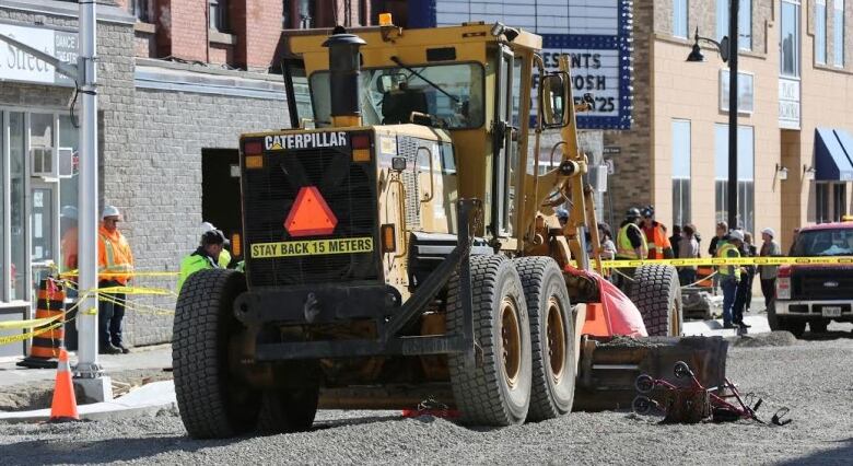 A walker sits next to a grader on a downtown street covered in gravel, with police tape strung around it. 