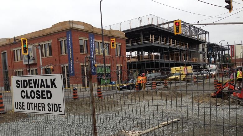 A construction site with fencing around it and a sign reading 'Sidewalk closed used other side'