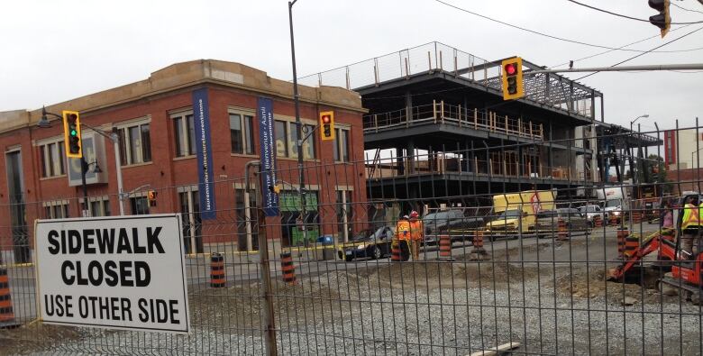 A construction site with fencing around it and a sign reading 'Sidewalk closed used other side'