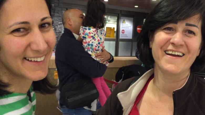 Two women smile, a man holds young child in the background, on the main floor of the Calgary International airport.