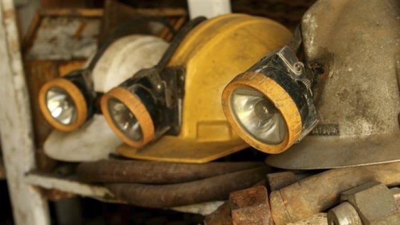 A picture of several miner's helmets that look like hard hats with flashlights clipped ot the front. One is yellow, one is white and one is metallic. They are sitting on pile of hoses and debris.