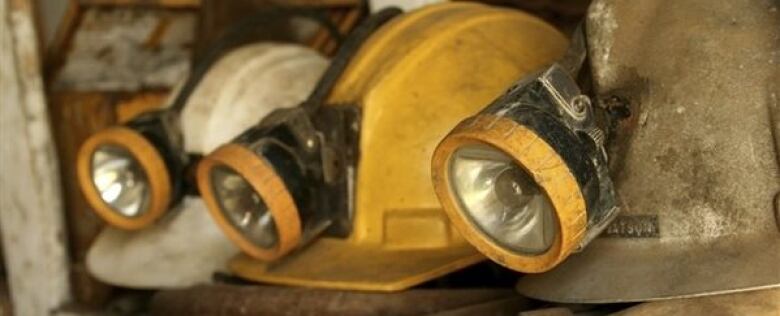 A picture of several miner's helmets that look like hard hats with flashlights clipped ot the front. One is yellow, one is white and one is metallic. They are sitting on pile of hoses and debris.