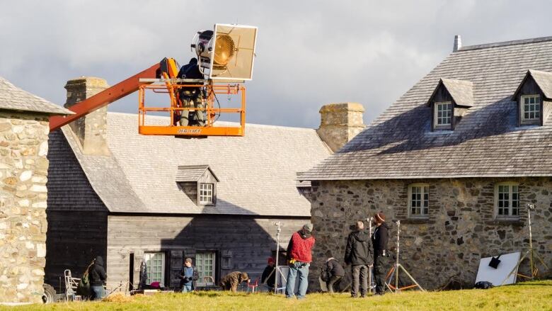 A film crew works with the stone buildings of the Fortress of Louisbourg in the background.