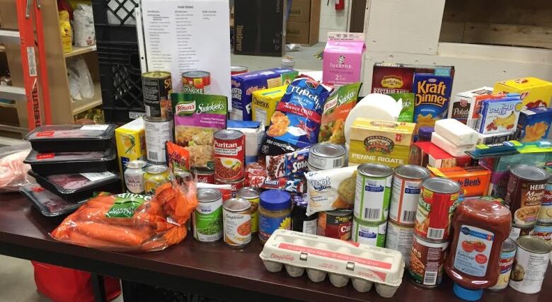 The contents of a food bank hamper are displayed on a table. There is an array of food, including eggs, carrots and canned goods. 