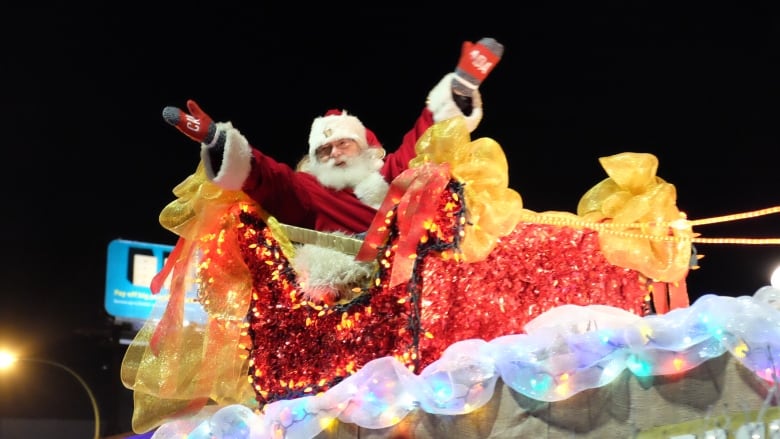 A man dressed as Santa Claus waves as he sits on a brightly coloured parade float.