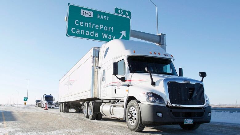 A semi-truck is driving under a sign that reads 